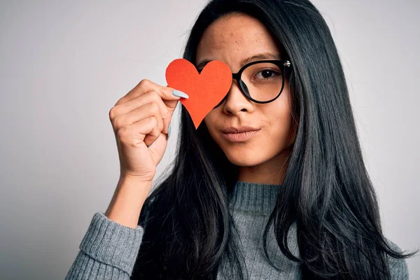 Young beautiful chinese woman holding paper heart over isolated white background with a confident expression on smart face thinking serious