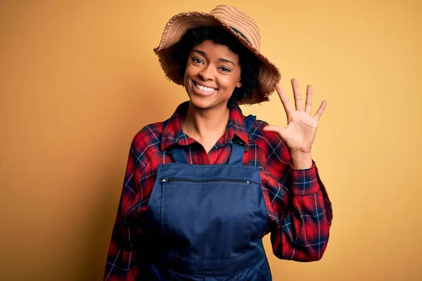 自信と幸せ笑顔ながら若いですアフリカ系アメリカ人のアフロ農家の女性との巻き毛のエプロンと帽子を身に着けていると指番号5で指摘します — ストック写真