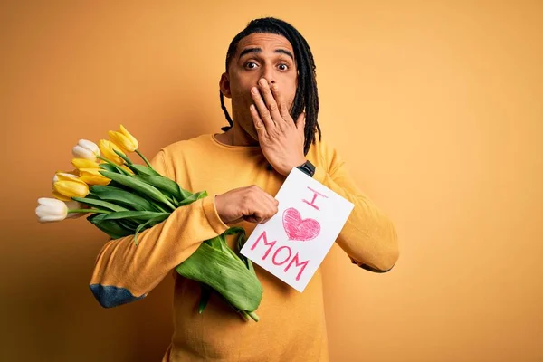 African american man holding love mom message paper and tulips celebrating mothers day cover mouth with hand shocked with shame for mistake, expression of fear, scared in silence, secret concept