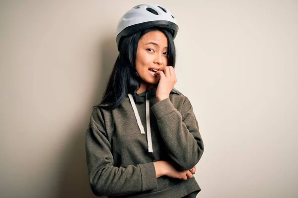孤立した白い背景の上に自転車のヘルメットを身に着けている若い美しい中国の女性は 口の爪をかむ上で手で強調し 緊張している 不安の問題 — ストック写真