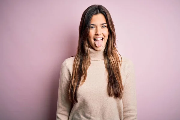 年轻美丽的女孩穿着宽松的毛衣 站在孤立的粉色背景上 带着滑稽的表情伸出舌头 情感概念 — 图库照片