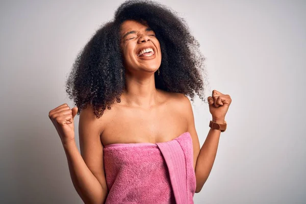 Young african american woman with afro hair wearing a body towel after beauty care shower very happy and excited doing winner gesture with arms raised, smiling and screaming for success. Celebration concept.