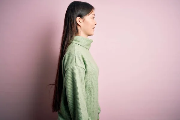 年轻美丽的亚洲女人 身穿绿色冬季毛衣 背景粉色 面向侧面 神采奕奕 面容自然 面带微笑自信 — 图库照片