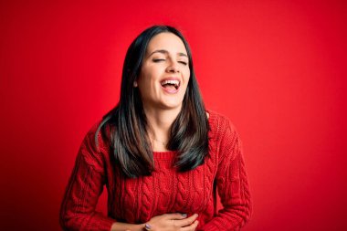 Mavi gözlü genç esmer kadın izole edilmiş kırmızı arka planda günlük süveter giyiyor ve kahkahalarla gülüyor..