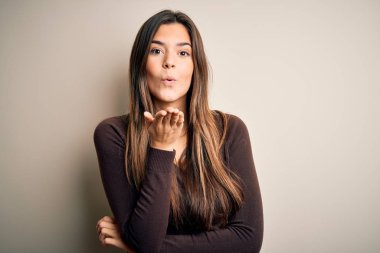 Young beautiful girl wearing casual sweater standing over isolated white background looking at the camera blowing a kiss with hand on air being lovely and sexy. Love expression.