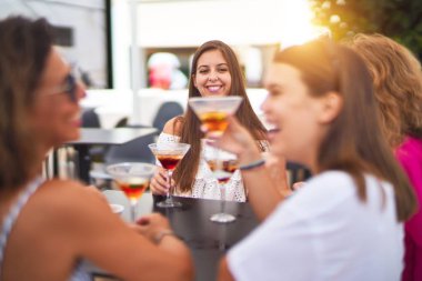 Güzel bir grup kadın restoranın terasında oturmuş kokteyller içiyor konuşuyor ve gülümsüyor.