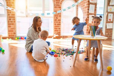 Güzel öğretmen ve bir grup çocuk anaokulunda bir sürü oyuncakla oynuyorlar.