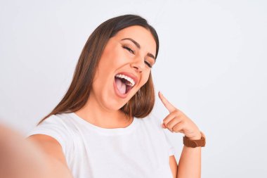 Güzel genç bir kadın beyaz arka plan üzerinde akıllı telefon kullanarak fotoğraf çekiyor. El ve parmak göstererek çok mutlu.