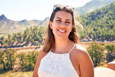 Genç, güzel bir kadın dağ manzarasında yaz tatilinin tadını çıkarıyor, gezgin kız mutlu gülümsüyor.