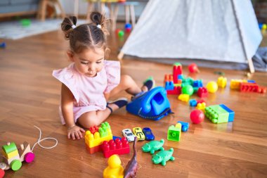 Young beautiful toddler sitting on the floor playing with vintage telephone at kindergaten