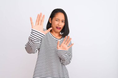 İzole edilmiş beyaz arka plan üzerinde duran çizgili tişört giyen genç Çinli kadın korku ifadesinden korkuyor ve dehşete kapılıyordu. El hareketlerini durdur, şok içinde bağır. Panik konsepti.