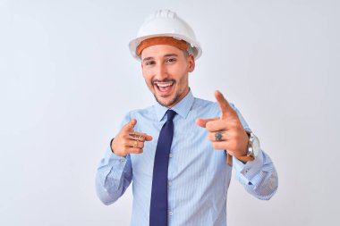Young business man wearing contractor safety helmet over isolated background pointing fingers to camera with happy and funny face. Good energy and vibes.