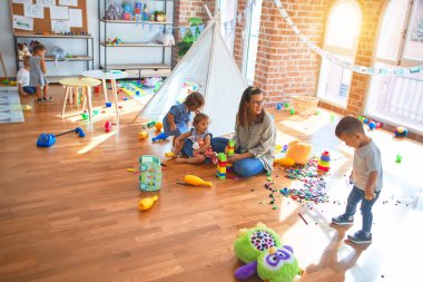 Güzel öğretmen ve bir grup çocuk anaokulunda bir sürü oyuncakla oynuyorlar.