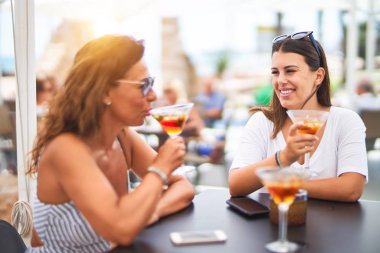Güzel anne ve kızı restoranın terasında oturmuş kokteyl içiyor ve gülümsüyor.