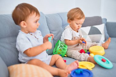 Kanepede oturup evde oyuncaklarla oynayan güzel bebekler.