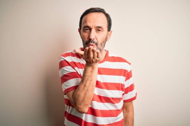 Orta yaşlı, beyaz tişörtlü bir adam izole edilmiş beyaz arka planda dikilip kameraya bakarak havada el sallayan ve güzel ve seksi bir öpücük veriyor. Aşk ifadesi.