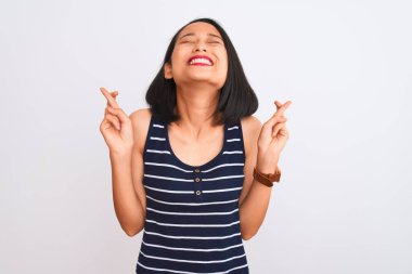 İzole edilmiş beyaz arka plan üzerinde duran çizgili tişört giyen genç Çinli kadın umut ve gözler kapalı bir şekilde gülümseyerek işaret ediyor. Şans ve batıl inanç..