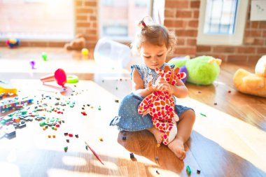 Sevimli bebek mutlu gülümsüyor. Yerde oturup anaokulunda bir sürü oyuncağın etrafında zürafa oyuncağıyla oynamak.