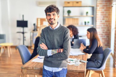 Group of business workers working together. Young handsome businessman standing smiling happy looking at the camera at the office