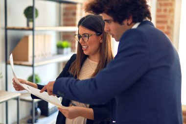 Two young beautiful business workers smiling happy and confident. Standing with smile on face working together speaking and reading documents at the office