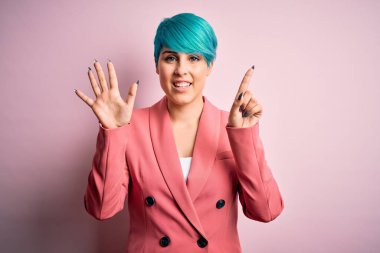 Young beautiful businesswoman with blue fashion hair wearing jacket over pink background showing and pointing up with fingers number six while smiling confident and happy.