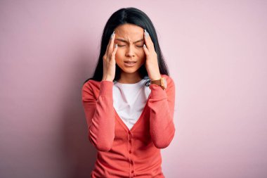 Genç, güzel, Çinli bir kadın stres yüzünden pembe arka plan üzerine günlük süveter giyiyor. Migren ağrısı..