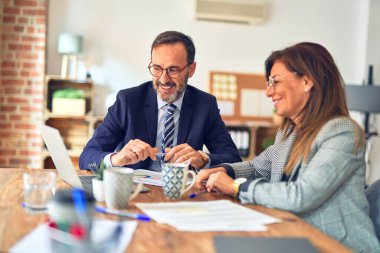 Mutlu ve kendinden emin gülümseyen iki orta yaşlı iş adamı. Ofiste dizüstü bilgisayarla gülümseyerek birlikte çalışıyoruz.