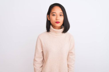 Balıkçı yaka kazak giyen genç Çinli kadın izole edilmiş beyaz arka planda dikiliyor yüzünde ciddi bir ifadeyle rahatlıyor. Basit ve doğal bir şekilde kameraya bakıyorsun..