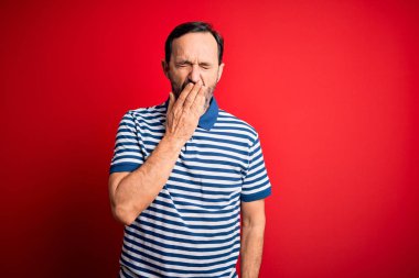 Middle age hoary man wearing casual striped polo standing over isolated red background bored yawning tired covering mouth with hand. Restless and sleepiness.