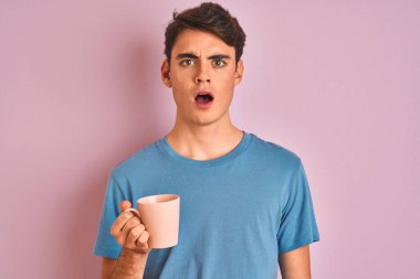 Genç bir çocuk pembe arka planda bir fincan kahve içiyor. Şaşırmış bir yüzle korkmuş ve korku ifadesinden heyecanlanmış.