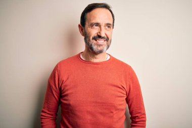 Middle age hoary man wearing casual orange sweater standing over isolated white background smiling looking to the side and staring away thinking.