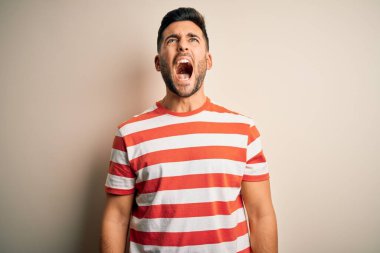Young handsome man wearing casual striped t-shirt standing over isolated white background angry and mad screaming frustrated and furious, shouting with anger. Rage and aggressive concept.