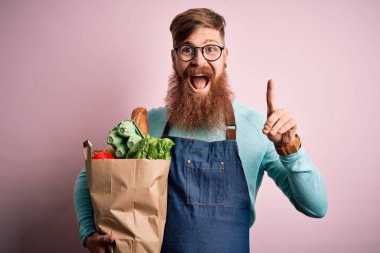 Kızıl saçlı, sakallı, elinde taze erzak taşıyan ve elinde bir fikir ya da soru işareti olan mutlu yüzlü bir süpermarket çalışanı.
