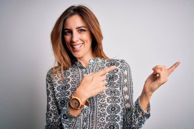 Young beautiful brunette woman wearing casual shirt standing over isolated white background smiling and looking at the camera pointing with two hands and fingers to the side.