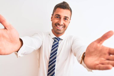 Genç yakışıklı, zarif bir iş adamı izole edilmiş arka planda kameraya bakıp sarılmak için kollarını açmış gülümsüyor. Mutluluğu kucaklayan neşeli bir ifade..