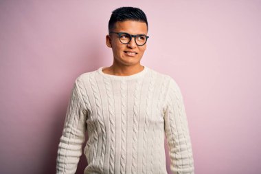 Beyaz günlük süveter giyen, pembe arka planda gözlüklü, yüzünde gülümseme, doğal bir ifade olan genç, yakışıklı Latin bir adam. Kendinden emin gülen.