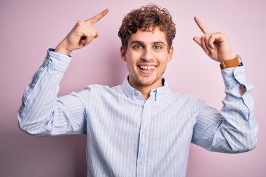 Young blond handsome man with curly hair wearing striped shirt over white background smiling pointing to head with both hands finger, great idea or thought, good memory