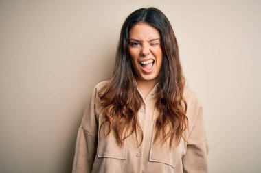 Genç, güzel, esmer, günlük gömlekler giyen, beyaz arka plan üzerinde duran, kameraya seksi bir ifadeyle bakan, neşeli ve mutlu yüzlü bir kadın..