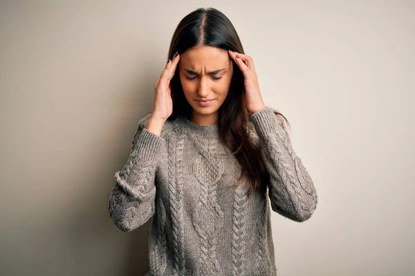 Young beautiful brunette woman wearing casual sweater over isolated white background with hand on head for pain in head because stress. Suffering migraine.