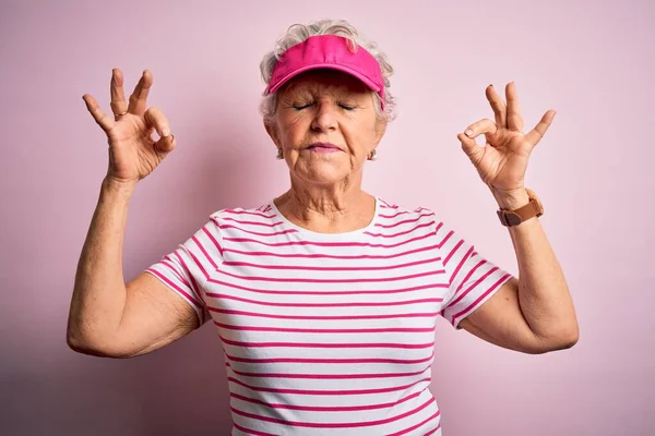站在孤立的粉色背景上 头戴运动帽的漂亮的大运动型女人放松 闭上双眼微笑 用手指做冥想动作 瑜伽概念 — 图库照片