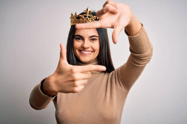 孤立した白い背景に黄金の女王の冠を身に着けている若い美しいブルネットの女性は幸せな顔を持つ手と指でフレームを作る笑顔 創造性と写真の概念 — ストック写真