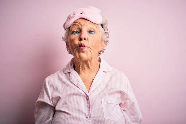 上了年纪的漂亮女人 戴着睡眠面具 披着睡衣 披着孤立的粉色背景 用嘴唇 疯狂和滑稽的姿势做着鱼脸 有趣的表达方式 — 图库照片