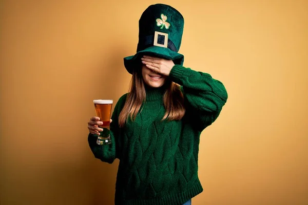 聖人の公園の日にビールの緑の帽子を飲むガラスを身に着けている若い美しい女性は笑顔と驚きのために目をカバー顔に手で笑っています ブラインドコンセプト — ストック写真