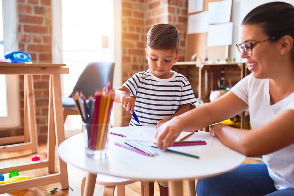 Beautiful teacher and toddler boy drawing draw using colored pencils at kindergarten