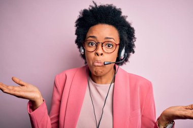 Genç Afrikalı Amerikalı çağrı merkezi operatörü, kıvırcık saçlı, kulaklık takan, kafası karışık, elleri ve kolları havada bir kadın. Şüphe kavramı.