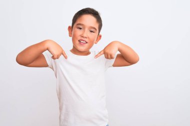 Güzel çocuk, izole edilmiş beyaz arka planda duran sıradan bir tişört giyiyor. Yüzünde bir gülümsemeyle, gururlu ve mutlu bir şekilde kendini işaret ediyor..