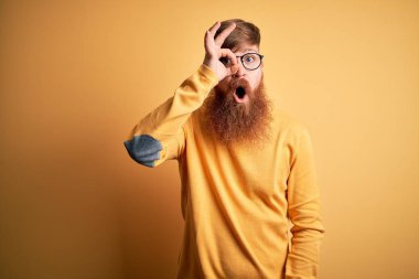 Sarıdan izole edilmiş arka planda gözlük takan yakışıklı, kızıl saçlı, güzel hareketler yapan, şaşkın bakışlı, gözleriyle parmaklarından bakan yakışıklı bir İrlandalı. İnançsız ifade.