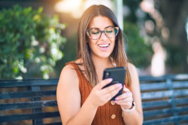 Mutlu ve kendinden emin gülümseyen genç ve güzel bir kadın. Yüzünde gülümsemeyle şehirde akıllı telefon kullanarak oturmak.
