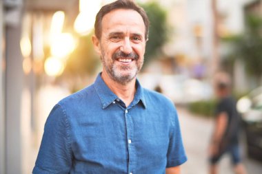 Orta yaşlı yakışıklı adam sokakta gülümsüyor.