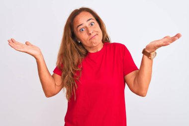 Orta yaşlı olgun bir kadın, beyaz soyutlanmış arka planda duruyor. Kolları ve elleri havada, kafası karışmış bir ifade. Şüphe kavramı.